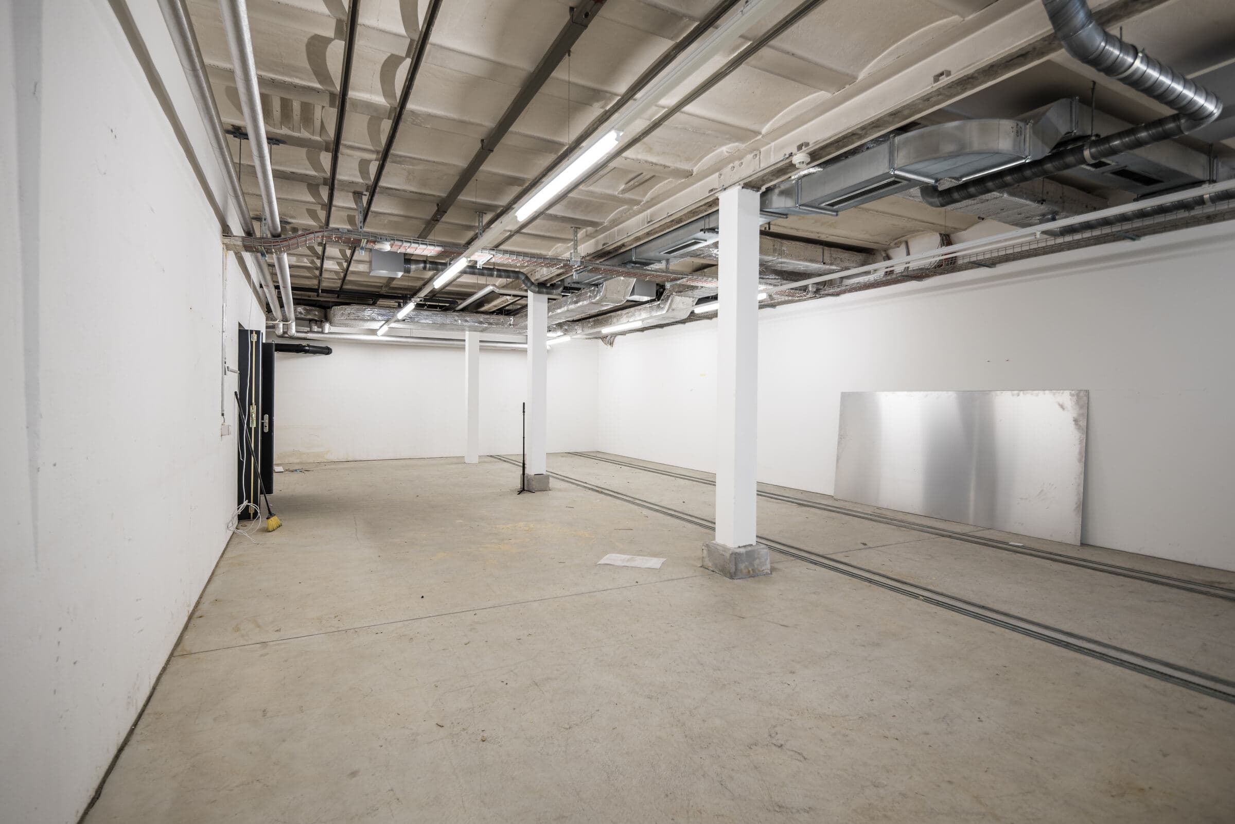 Untergeschoss mit Betonboden, Leitungen an der Decke und einer Metallplatte an der Wand
